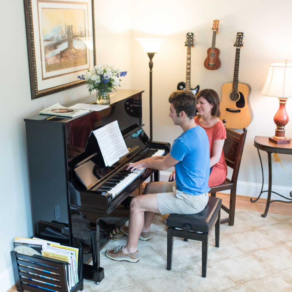 older teen male student sits on the piano bench while his teacher sits beside him